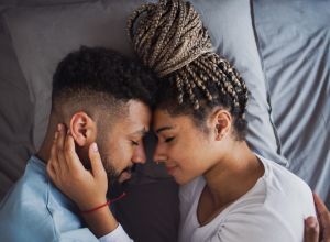 Top view portrait of young couple on bed indoors at home, cuddling, eyes closed.